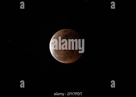 L'ombra della terra cade in parte attraverso una luna piena, mentre si erge sopra un lato di montagna durante un'eclissi lunare totale vista da Anilao nella provincia di Batangas, a sud di Manila, Filippine. Foto Stock