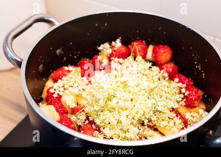 Fragole e fiori di sambuco marmellata cottura in pentola nera. La foraggazione primaverile conserva l'ispirazione della ricetta. Primo piano, vista laterale. Foto Stock