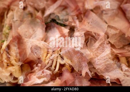 Primo piano e vista macro al katsuobushi, fiocco di bonito che sulla cima di Takoyaki o polpo giapponese palle, servire su scatola di carta bianca. Foto Stock