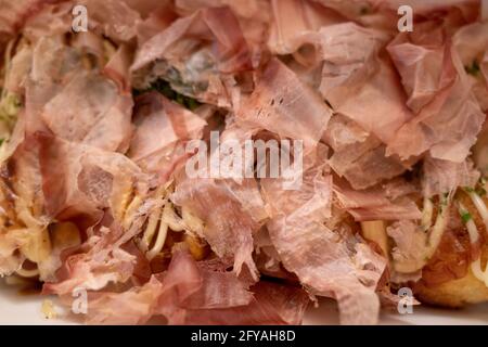 Primo piano e vista macro al katsuobushi, fiocco di bonito che sulla cima di Takoyaki o polpo giapponese palle, servire su scatola di carta bianca. Foto Stock