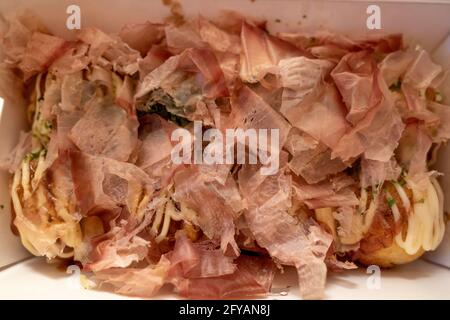 Primo piano e vista macro al katsuobushi, fiocco di bonito che sulla cima di Takoyaki o polpo giapponese palle, servire su scatola di carta bianca. Foto Stock