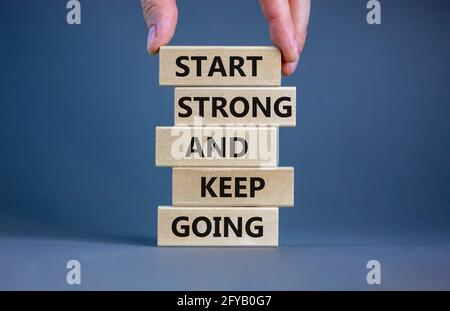 Inizia forte e continua a andare simbolo. Le parole di concetto "Start strong and Keep Going" su blocchi di legno su uno splendido sfondo grigio. Mano uomo d'affari. Autobus Foto Stock