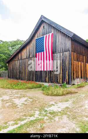 Castroville, Texas, Stati Uniti. 12 aprile 2021. Grande bandiera americana su un fienile nella regione collinare del Texas. Foto Stock