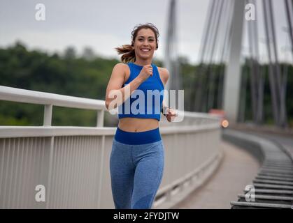 Fit giovane donna in abbigliamento sportivo jogging sul ponte durante il giorno. Concetto di stile di vita sano e attivo Foto Stock