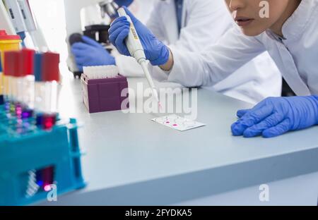 Giovane scienziato che utilizza moderne attrezzature mediche in laboratorio. Donna con pipetta che prepara i campioni per il microscopio. Foto Stock