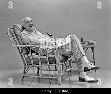 ANNI '30 1940 UOMO VESTITO ALLA MODA SEDUTA IN SEDIA DI RATTAN FUMO UNA RIVISTA DI GIORNALI DI LETTURA PIPE SORRIDENTE GUARDANDO LA MACCHINA FOTOGRAFICA - S2904 HAR001 HARS ELDER STUDIO SHOT PIPE HEALTHINESS HOME LIFE COPY SPACE FULL-LENGTH PERSONS MASCHI CONFIDENZA SENIOR MAN SENIOR ADULT B&W OCCHIO CONTATTO RATTAN FELICITÀ VECCHIAIA OLDSTERS OLDSTER TEMPO LIBERO STILI E PUNTE ANZIANI ALLA MODA OXFORD SPETTATORE ELEGANTE UOMO ANZIANO COLORI A DUE TONALITÀ CHE CONTRASTANO LA MODA RELAX PUNTE ALA NERO E BIANCO CASUAL CAUCASICO ETNIA HAR001 VECCHIO STILE Foto Stock