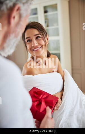 Bella signora caucasica avvolta in coperta guardando al non riconosciuto uomo in appartamento moderno Foto Stock