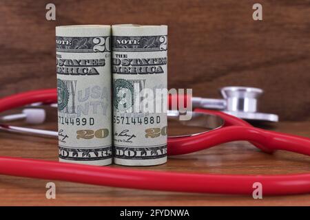 Il denaro americano messo con stetoscopio rosso su sfondo di legno riflette investimenti e costi nelle industrie sanitarie, tra cui infermieri e. medico Foto Stock