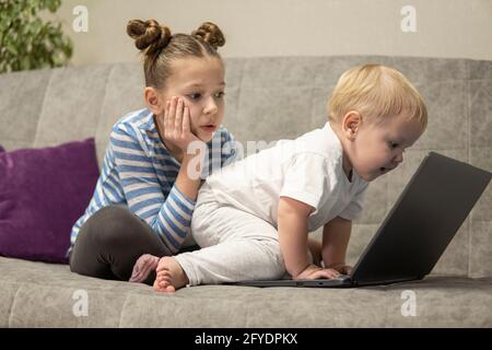 Bambina e ragazzo carino che usano il computer portatile insieme, guardando lo schermo, guardando i cartoni animati o giocando online, sorella e fratello, fratelli seduti su comfor Foto Stock