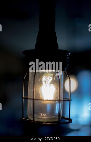 Elegante luce elettrica retrò in griglia metallica protettiva su sfocata sfondo blu Foto Stock