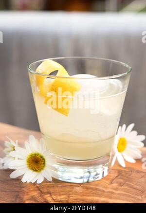 Un cocktail di ginocchia, vodka o gin con limone e miele, guarnito con scorza di limone e qualche margherita. Foto Stock