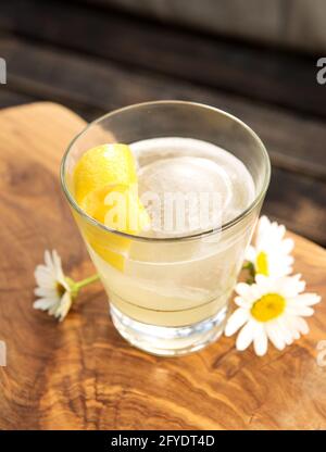 Un cocktail di ginocchia, vodka o gin con limone e miele, guarnito con scorza di limone e qualche margherita. Foto Stock