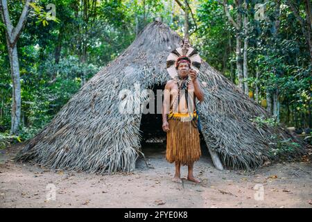 Sciaman della tribù Pataxó, indossando un headdress di piuma e fumando un tubo. Brasiliano indiano guardando la macchina fotografica Foto Stock