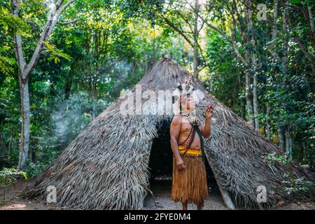 Sciaman della tribù Pataxó, indossando un headdress di piuma e fumando un tubo. Indiano brasiliano guardando la destra Foto Stock