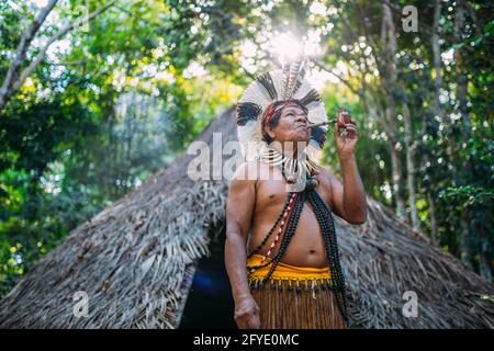 Sciaman della tribù Pataxó, indossando un headdress di piuma e fumando un tubo. Indiano brasiliano guardando la destra Foto Stock