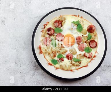 Tortilla con formaggio, patate, salsicce e uova fritte su un piatto rotondo su fondo grigio chiaro. Vista dall'alto, disposizione piatta Foto Stock