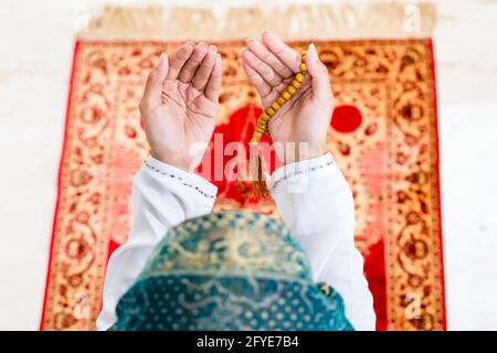 Musulmani asiatici donna orante sul tappeto con catena di perline indossando vestiti tradizionali Foto Stock