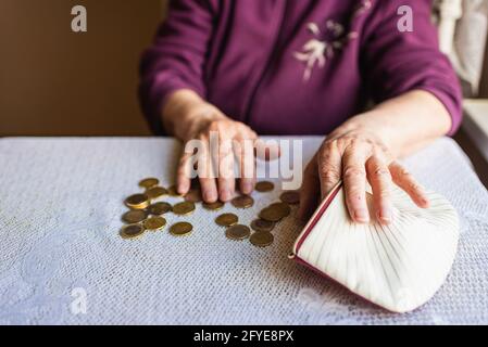 Donna anziana preoccupata seduta a casa e contando monete rimanenti.old donna seduta miserabilmente al tavolo a casa e contando monete rimanenti fra Foto Stock