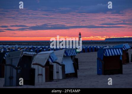 28 maggio 2021, Meclemburgo-Pomerania occidentale, Warnemünde: Il sole che sorge colora il cielo dietro il faro sul molo del Mar Baltico rosso-arancio. In primo piano ci sono sedie da spiaggia vuote sulla costa. Il Servizio Meteo Tedesco (DWD) presenta il suo equilibrio meteorologico per la primavera. Foto: Jens Büttner/dpa-Zentralbild/dpa Foto Stock