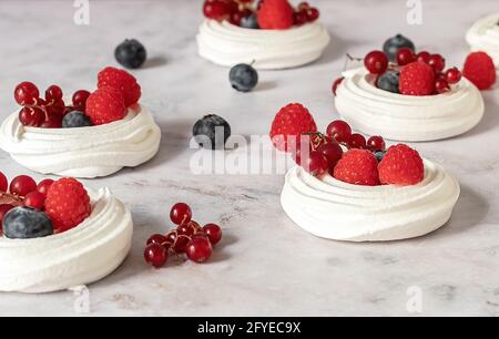 Meringhe o mini Pavlova. Dessert dolce decorato con frutti di bosco diversi. Foto Stock