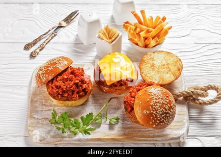 Panini Slippy Joe su brioche panini serviti con patatine fritte su un bordo di legno bianco, primo piano, cucina americana Foto Stock