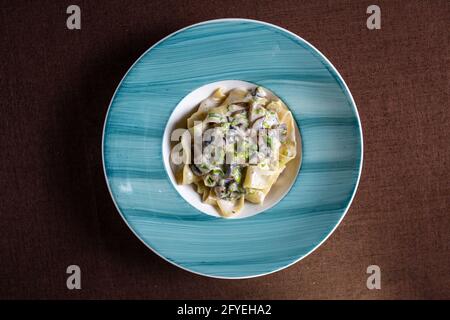 pasta con formaggio, erbe e funghi in un piatto blu vista dall'alto. Foto Stock