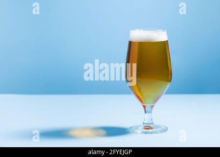 Birra rinfrescante in un bicchiere su sfondo blu con un'ombra dura. Spazio di copia. Foto Stock