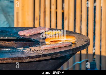 Salsicce alla griglia, bistecche e fette di pane su un'ampia griglia all'aperto. Festa del barbecue nel parco cittadino. Foto Stock
