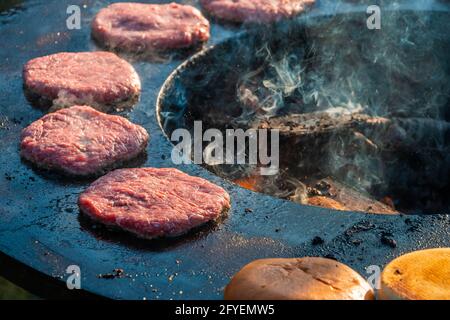 Le polpettine di manzo e gli hamburger vengono grigliati su una grande griglia rotonda all'aperto che brucia il legno, primo piano. Festa del barbecue nel parco cittadino. Via veloce Foto Stock