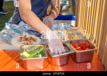 Uno chef professionista riempie i gyros di ripieno. Festa del barbecue nel parco cittadino. Cucina greca, fast food di strada. Foto Stock