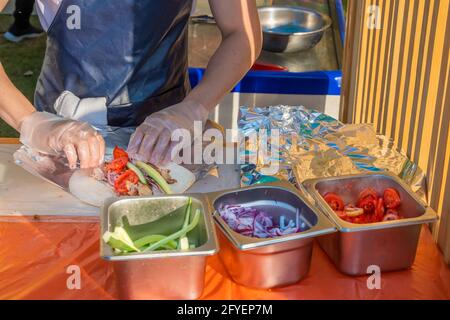 Uno chef professionista riempie i gyros di ripieno. Festa del barbecue nel parco cittadino. Cucina greca, fast food di strada. Foto Stock