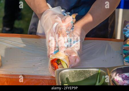 Uno chef professionista riempie i gyros di ripieno. Festa del barbecue nel parco cittadino. Cucina greca, fast food di strada. Foto Stock