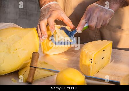 Le mani del negoziante tagliano da vicino una testa di formaggio. Formaggio artigianale in un mercato di strada. Caseificio tagliando il formaggio nel suo laboratorio. Festival del cibo in Foto Stock