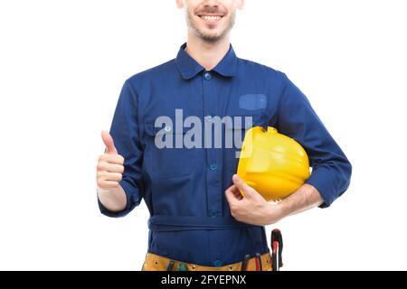 Orizzontale medio ritratto di successo bel giovane adulto caucasico costruzione ingegnere indossando uniforme blu che tiene hardhat, sfondo bianco Foto Stock