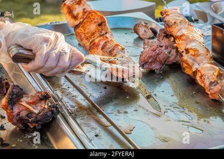 Kebab shish fritto su spiedini al banco di un ristorante di strada. Festa del cibo nel parco cittadino. Street fast food. Messa a fuoco selettiva, profondità superficiale o Foto Stock
