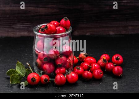 Frutto di rosa in vaso di vetro su ardesia nera, sfondo naturale con bacche rosse Foto Stock