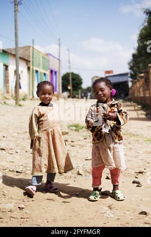 Bambini etiopi nella strada del villaggio di Hawzien, due bambina vestita di stracci e un ragazzino che rotola un pneumatico. Regione del Tigray, Etiopia Foto Stock