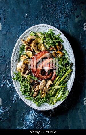 Insalata di pesce. Tentacoli grigliati di polpo, sardine e cozze su piatto di ceramica blu serviti con insalata di rucola, zucchine e asparagi Foto Stock