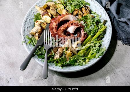 Insalata di pesce. Tentacoli grigliati di polpo, sardine e cozze su piatto di ceramica blu serviti con insalata di rucola, zucchine e asparagi Foto Stock