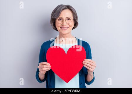 Ritratto fotografico di felice donna d'affari sorridente tenendo il cuore rosso cartolina sagomata isolata su sfondo grigio Foto Stock