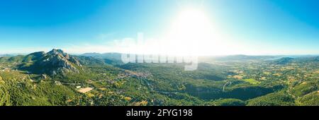 Vista dall'alto, splendida vista aerea del villaggio di San Pantaleo circondato da alcune montagne di granito, vegetazione verde e il Mar mediterraneo Foto Stock