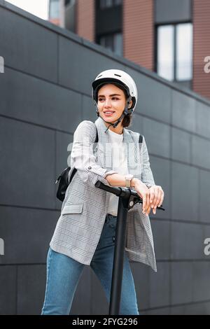 Uomo d'affari appoggiato su scooter elettrico e guardando via. Ritratto di giovane femmina che tiene scooter all'aperto. Foto Stock