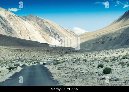 Una strada in cemento verso splendide montagne rocciose e cielo blu con cime di Himalaya, Leh, Ladakh, Jammu e Kashmir, India Foto Stock