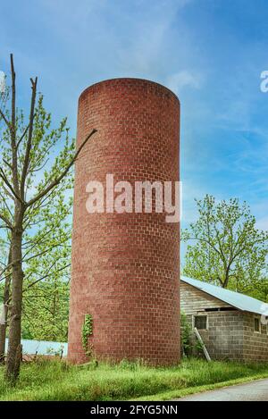 Vecchio silo di mattoni contro un bel cielo blu accanto ad un edificio isolato. Foto Stock