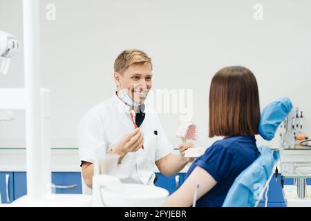 Dentista che mostra la corretta igiene dentale utilizzando mock-up di scheletro di denti. Medico stomatologo che spiega la corretta igiene dentale per il paziente che tiene un campione di mandibola umana con spazzolino da denti. Foto Stock