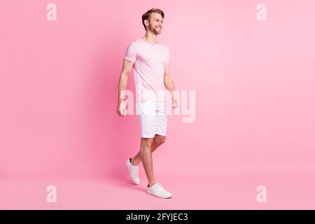 Foto di bella carina giovane gentiluomo vestito casual t-shirt a piedi sorridente aspetto vuoto spazio isolato sfondo di colore rosa Foto Stock
