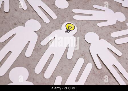 Figure scolpite di persone su sfondo grigio. Lampadina gialla invece di cervello. Persona intelligente nella società, talento, capacità di generare idee. Foto Stock