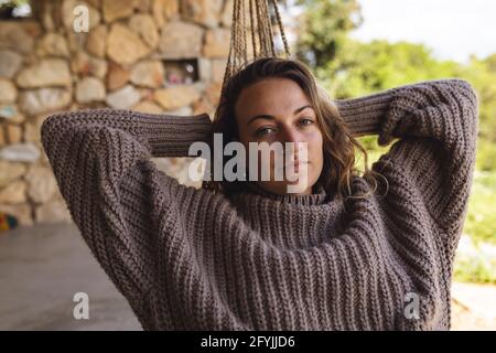 Ritratto di donna caucasica premurosa che si rilassa in amaca sulla terrazza cottage, guardando alla macchina fotografica Foto Stock