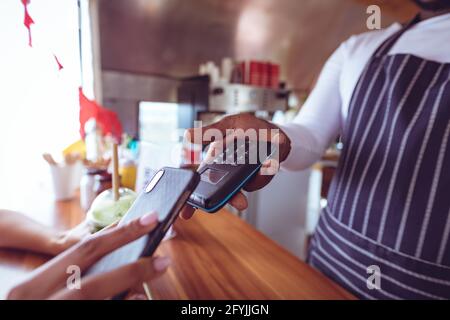 La sezione centrale dell'uomo afroamericano in camion di alimento che prende smartphone terminale di attesa del pagamento Foto Stock