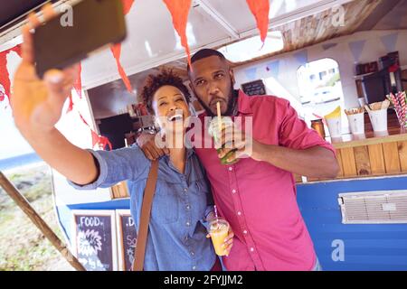 Sorridente coppia diversa prendendo selfie con smartphone e bere in camion al mare Foto Stock